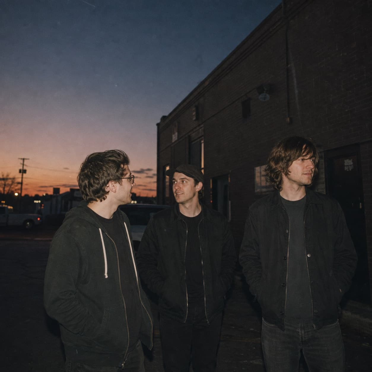 Three musicians standing outside a modest venue at dusk